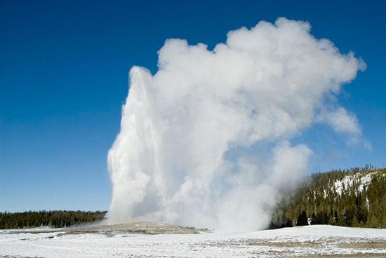 clouds in the sky over a snow covered slope with Old Faithful in the background