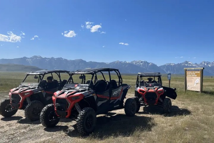 Three off-road vehicles parked on grassy field with mountains in background.
