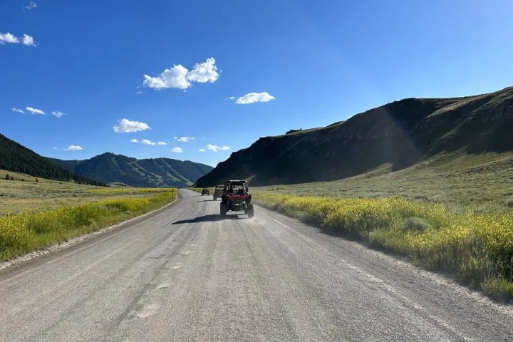 Off-road vehicles on a scenic mountain road under a clear blue sky.
